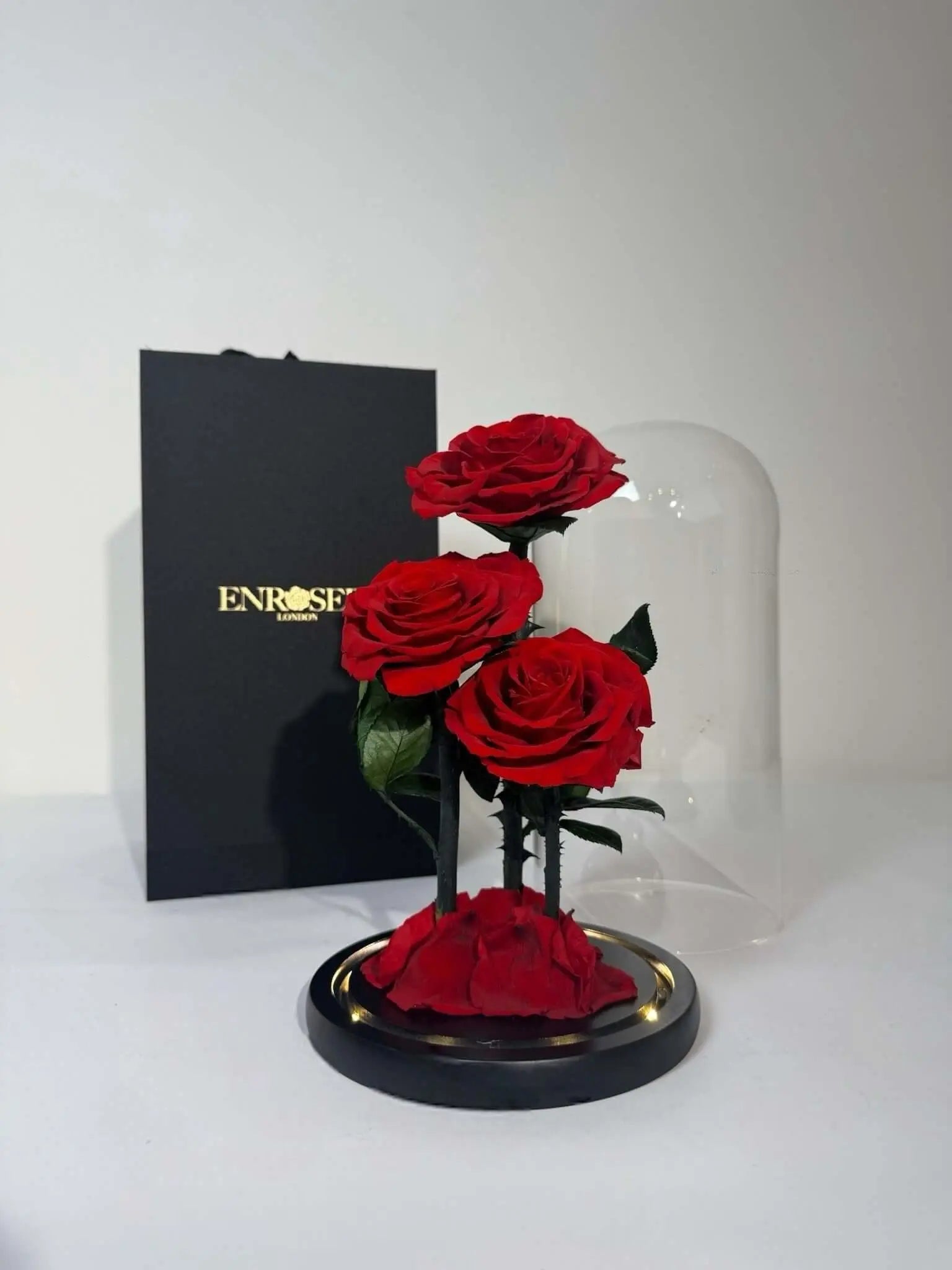 Triple Elegance Grandi with three red roses under glass dome, featuring elegant gift box and warm LED lighting.